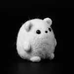 A small white felt buddy with black bead eyes, sitting on a black floor